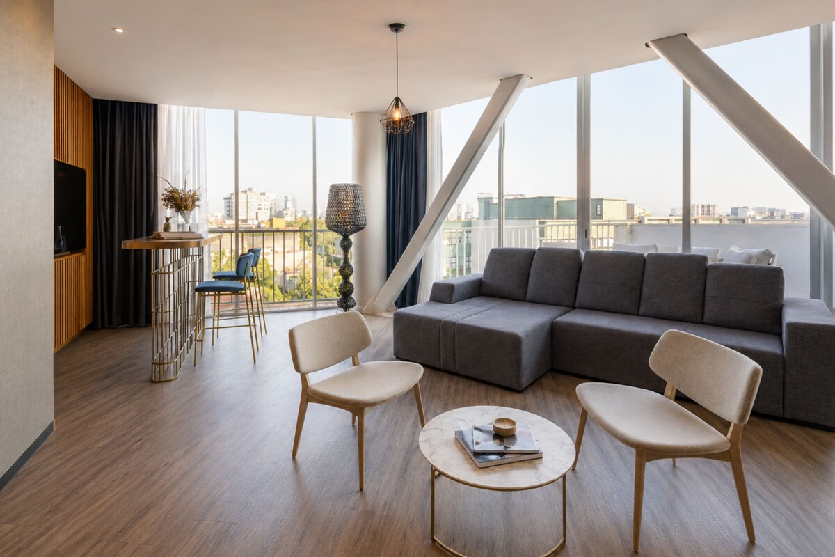 Una sala moderna con un sofá seccional, dos sillones, una mesa de centro, un televisor y un balcón con vistas a la ciudad.