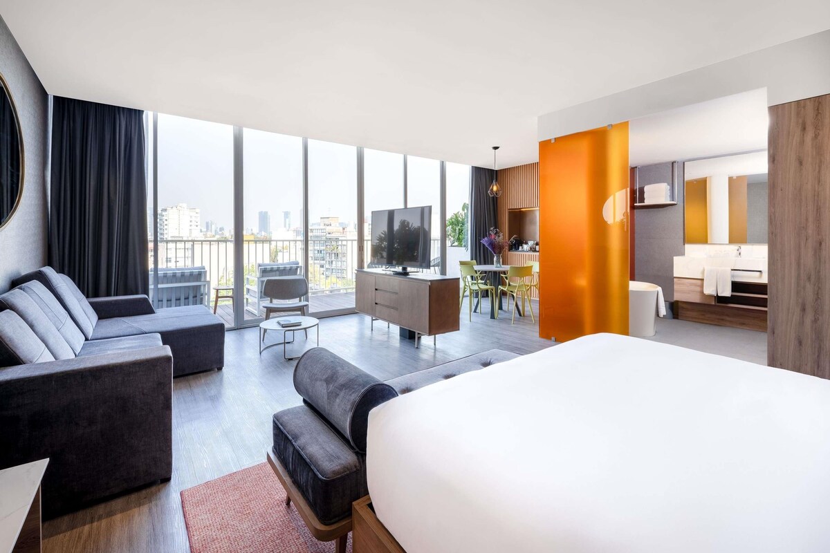 Una habitación de hotel moderna con una cama grande, un sofá, una zona de comedor y un televisor.