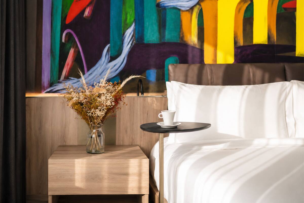 Una habitación de hotel con una cama, una mesita con una taza y un jarrón con flores secas.