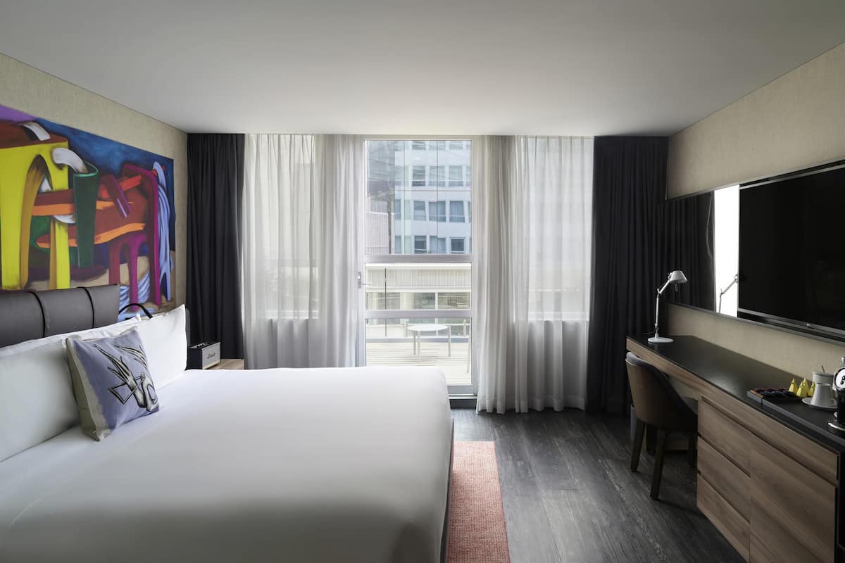 Een hotelkamer met een bed, een bureau, een televisie en een groot raam met gordijnen.