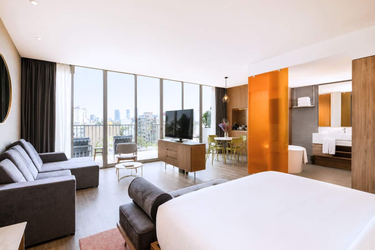 Een moderne hotelkamer met een groot bed, een televisie, een zithoek en uitzicht over de stad.