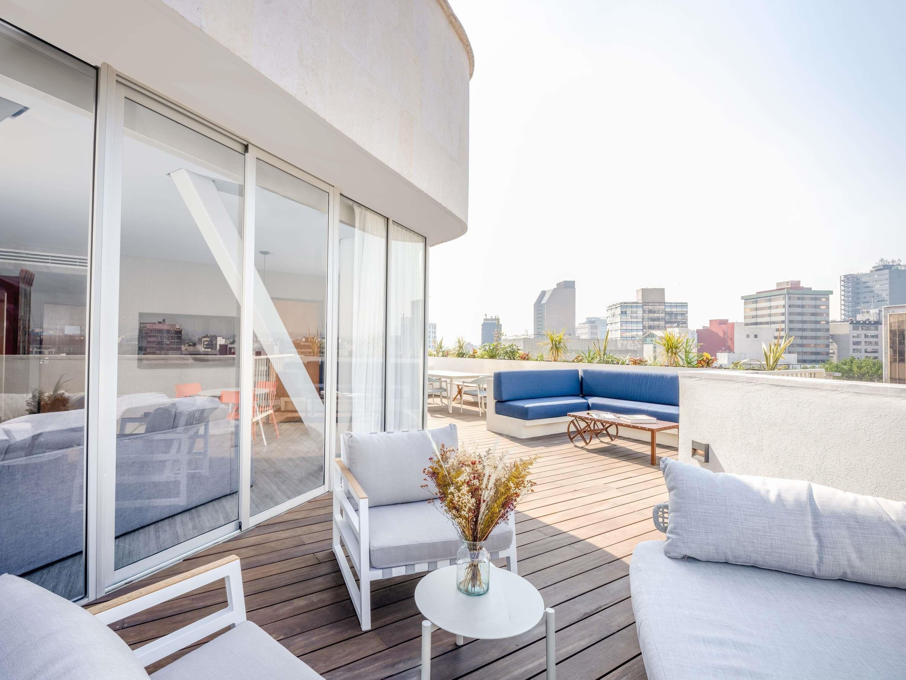 A modern rooftop terrace with a sofa, chairs, and a table.