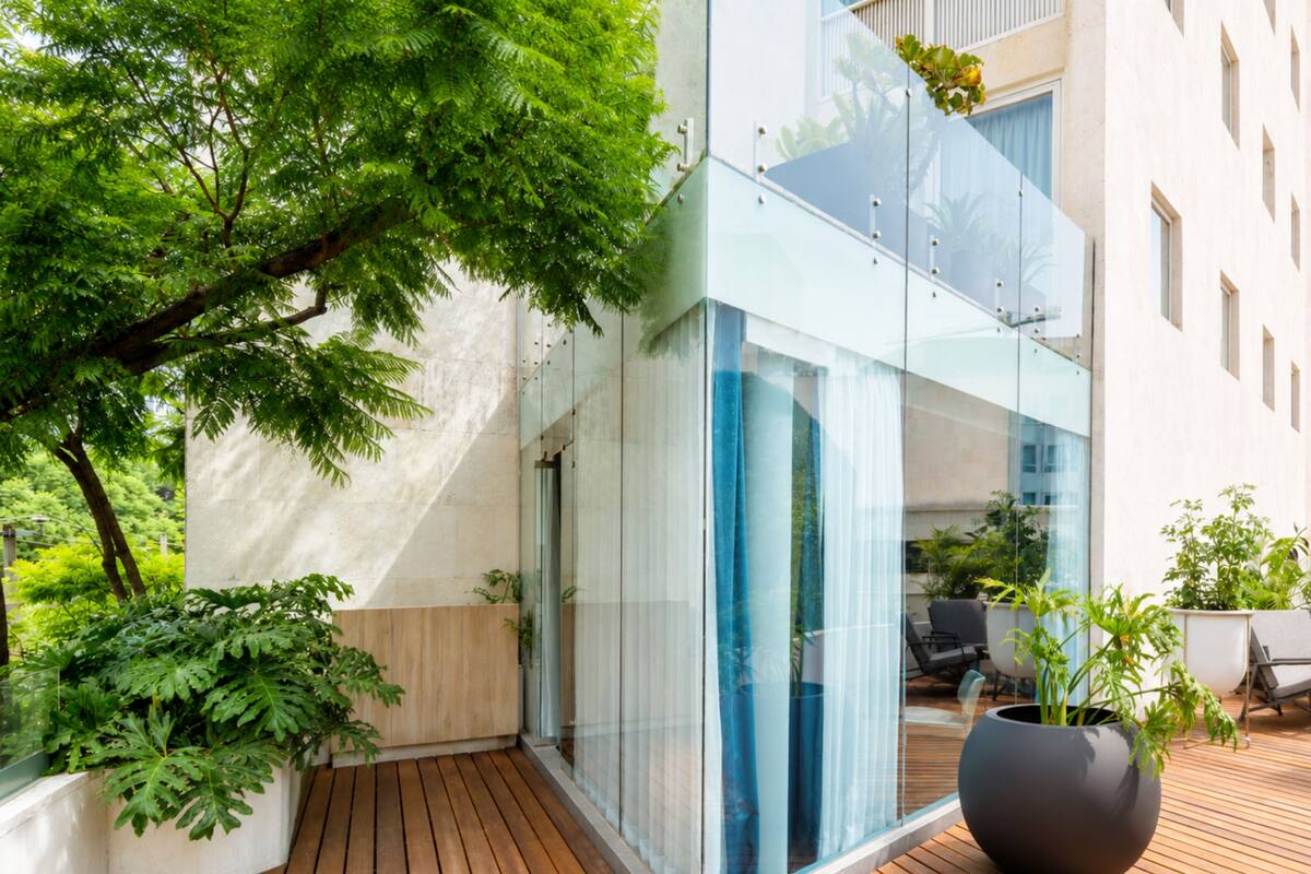 Een modern gebouw met een glazen gevel, houten terras en potplanten.
