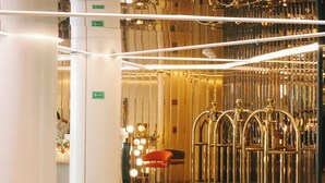 Un hall d’hôtel avec un grand piano, un fauteuil rouge et un ascenseur doré.