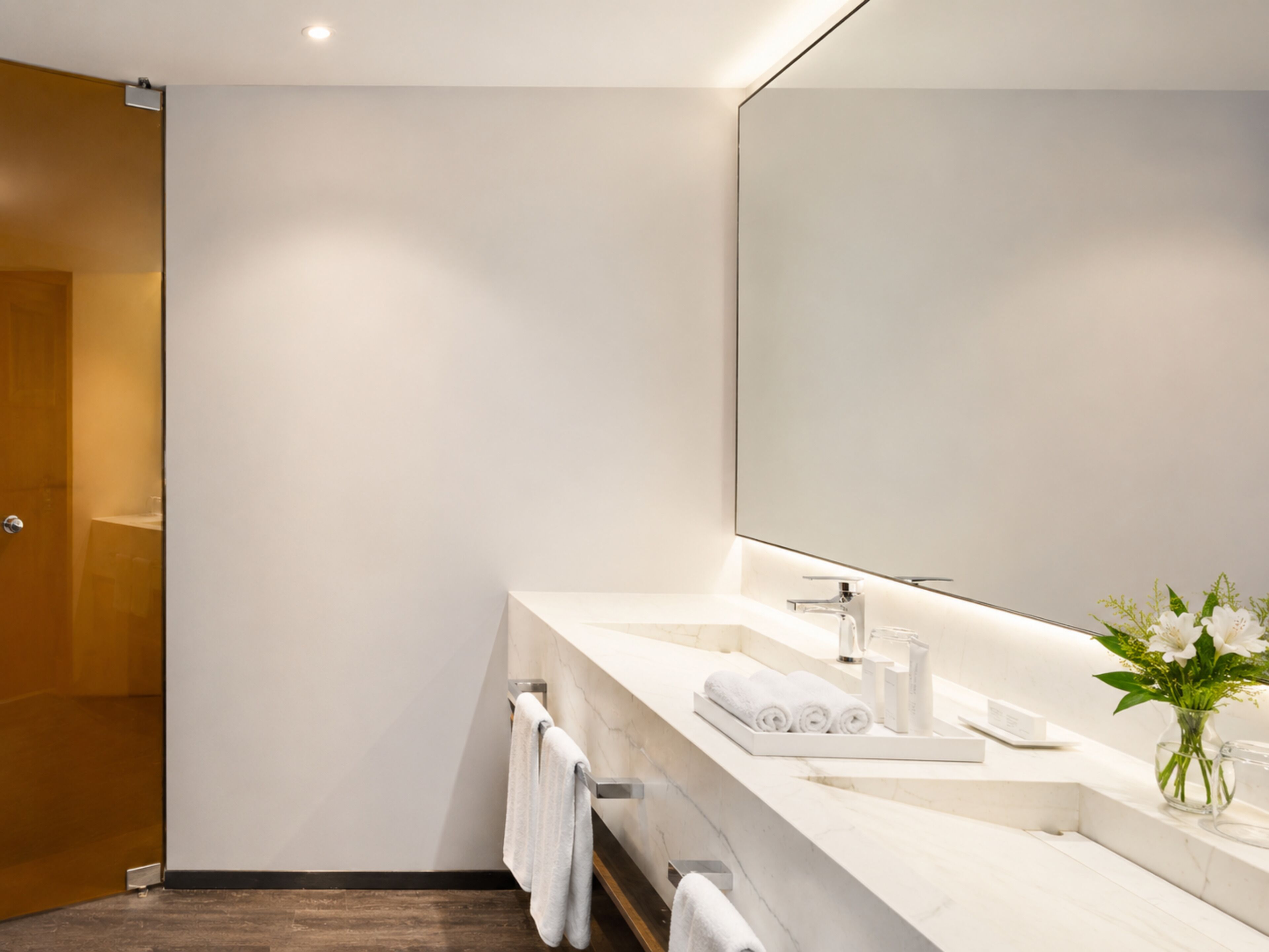 A modern bathroom with a large mirror, white marble countertop, and a glass shower enclosure.