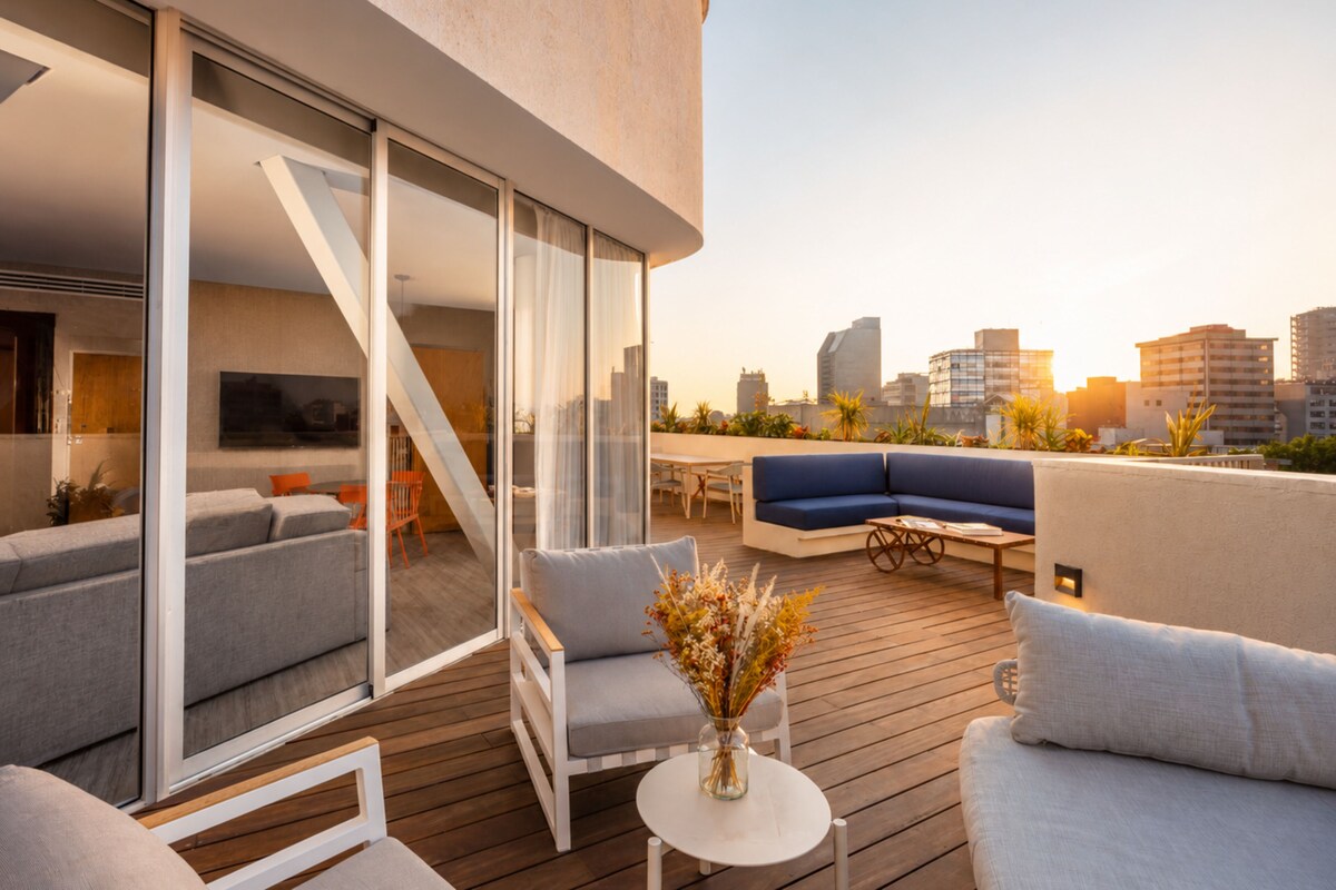 Un espacio exterior moderno con sofá, sillas y una mesa, con vistas a un paisaje urbano.