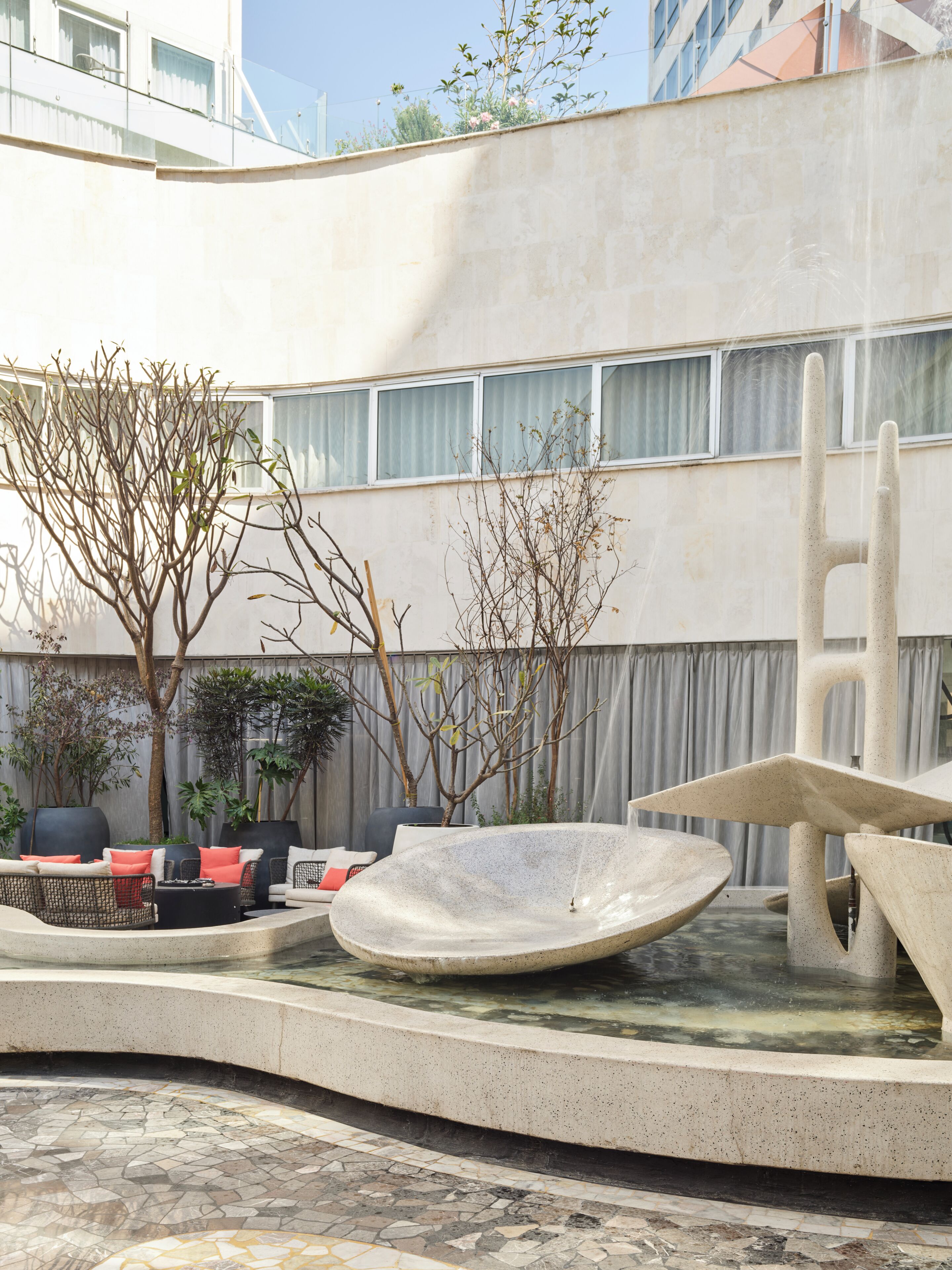 A courtyard with a water feature, seating area, and a building with large windows.
