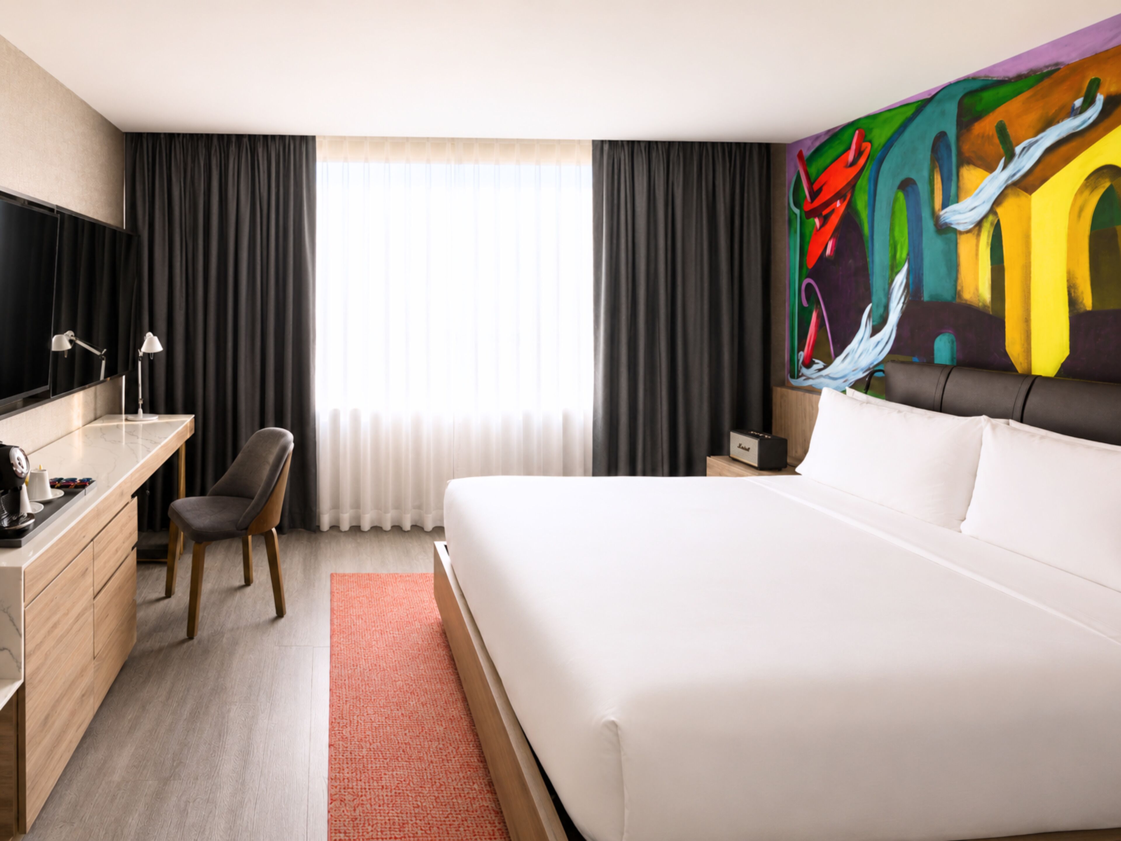 Habitación de hotel con cama, escritorio, silla y un cuadro abstracto grande en la pared.