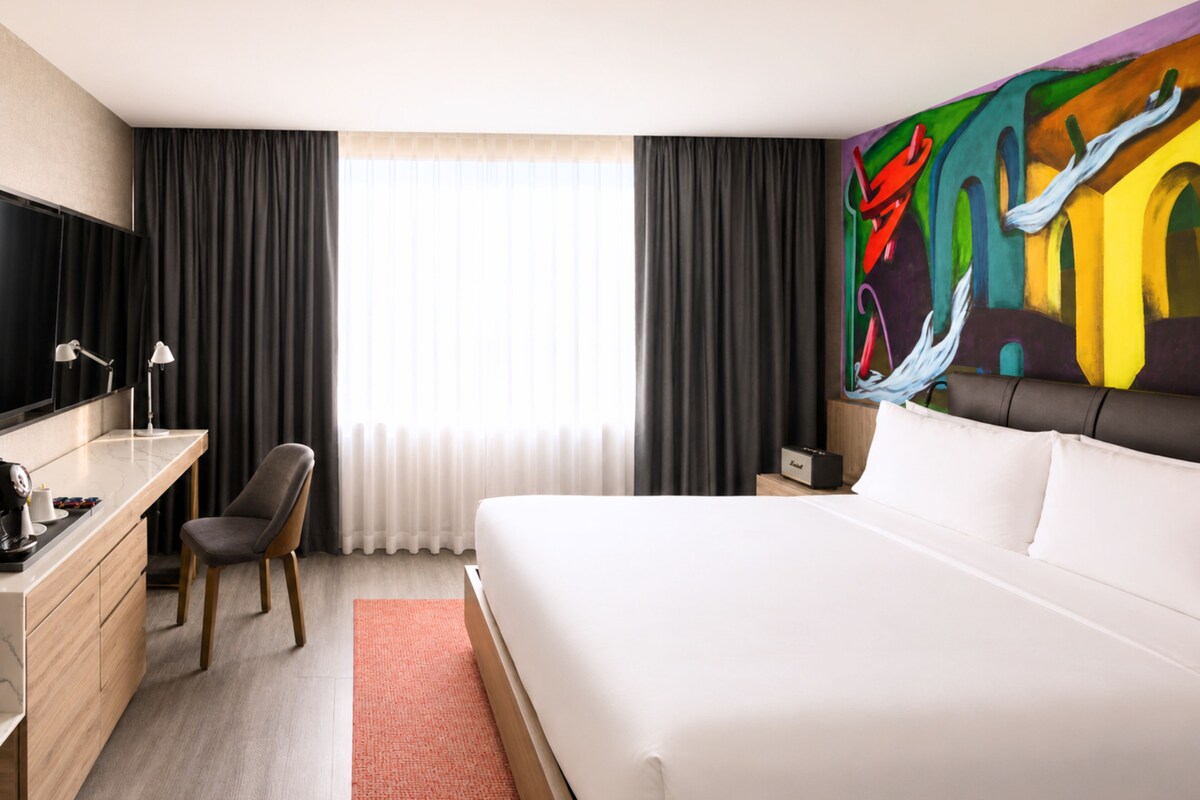 Habitación de hotel con cama, escritorio, silla y un cuadro abstracto grande en la pared.