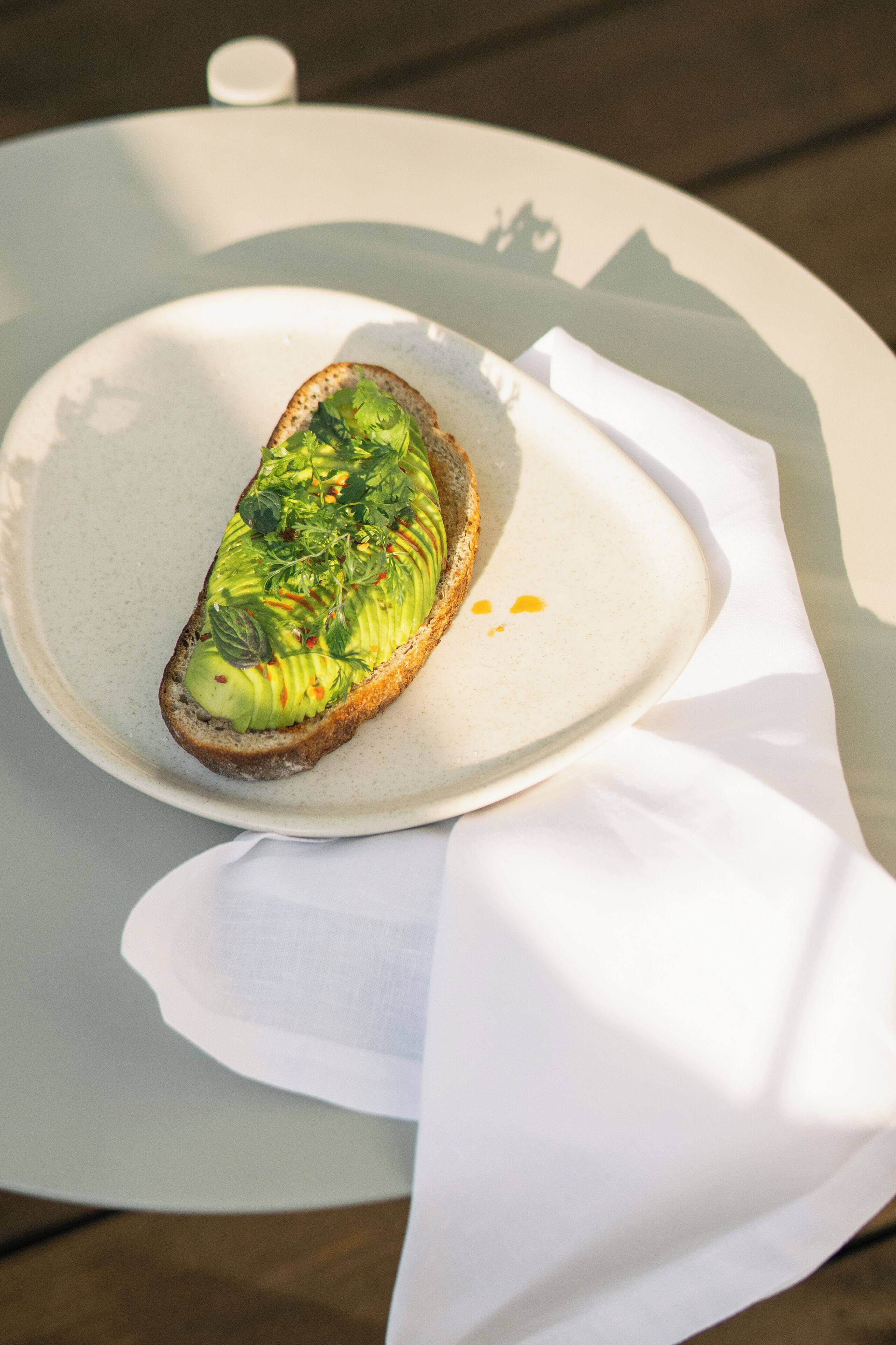 Een bord met een sneetje brood belegd met avocado en groenten, geplaatst op een wit bord met een servet.
