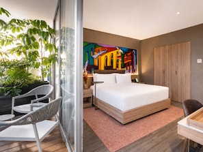 Una habitación de hotel moderna con una cama grande, un separador de vidrio, una zona de comedor y un cuadro abstracto y llamativo en la pared.
