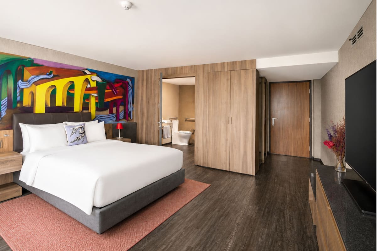 Een moderne hotelkamer met een groot bed, een flatscreen televisie, een houten garderobe, een badkamer en een kleurrijke muurschildering.