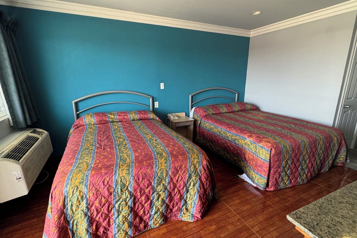 Quarto com duas camas, janela com cortinas, aquecedor e uma pequena mesa.