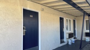 A row of hotel rooms with numbered doors, a covered walkway, and a few buckets on the ground. - Hiland Motel (Long Beach)