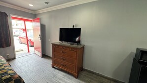 A hotel room with a wooden dresser, a television on top, a bed with a colorful quilt, and a door leading outside. - Hiland Motel (Long Beach)