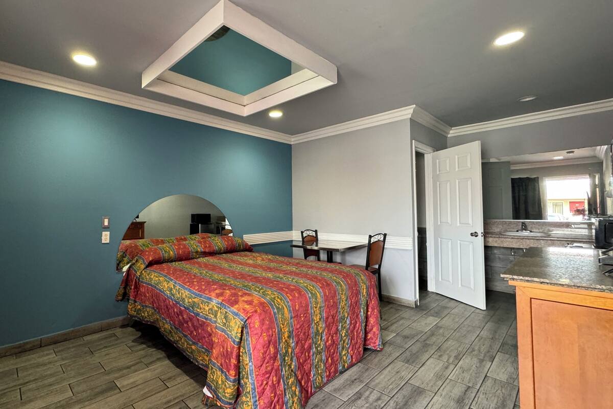 Quarto com cama, escrivaninha e cozinha compacta.