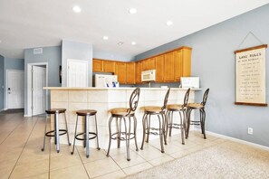A kitchen with wooden cabinets, a white countertop, and bar stools.