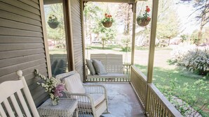 A porch with two wicker chairs and a bench, a small table with a vase of flowers, and hanging planters with red flowers. - Bridgewalk Estate | a Wanderlust Abodes property (Central Lake)