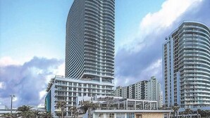 A modern high-rise building with a curved facade, surrounded by other high-rise buildings and palm trees. - Amazing Ocean Views at LYFE Resort @rent4us (Hollywood)