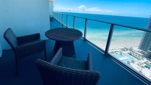 A balcony with wicker furniture, a round table, and a view of the ocean and a resort area. - Amazing Ocean Views at LYFE Resort @rent4us (Hollywood)