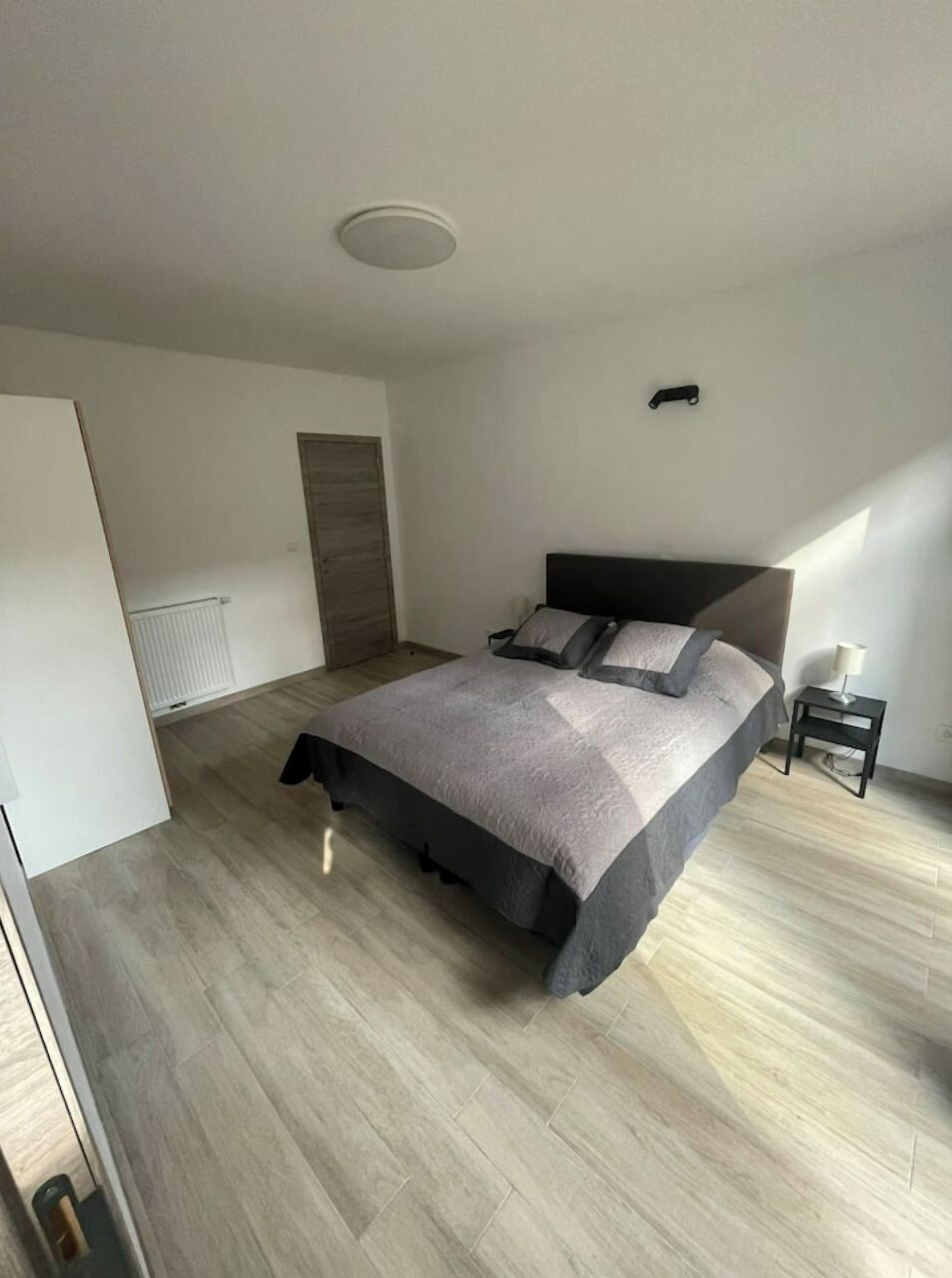 Een moderne slaapkamer met een groot bed, een nachtkastje, een radiator en een deur.