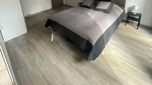 A modern bedroom with a large bed, a bedside table, a radiator, and a door.