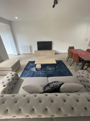 A modern living room with a grey tufted sofa, a wooden coffee table, and a blue rug. - Appartement 3 Chambres Avec Jardin Privatif (Charleroi)