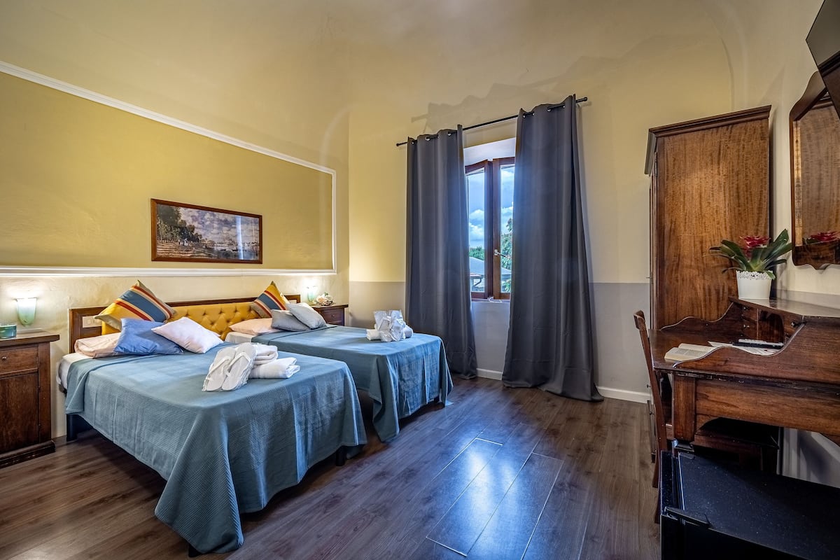 Une chambre avec deux lits, un bureau en bois, un miroir et une fenêtre avec des rideaux.