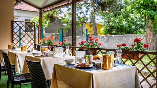 An outdoor dining area with tables set for breakfast, featuring croissants, fruit, and coffee. - Hotel Minerva (Pisa)