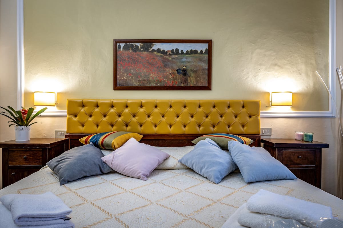 Une chambre d’hôtel avec une tête de lit capitonnée, un tableau au-dessus du lit et deux lampes de chevet.