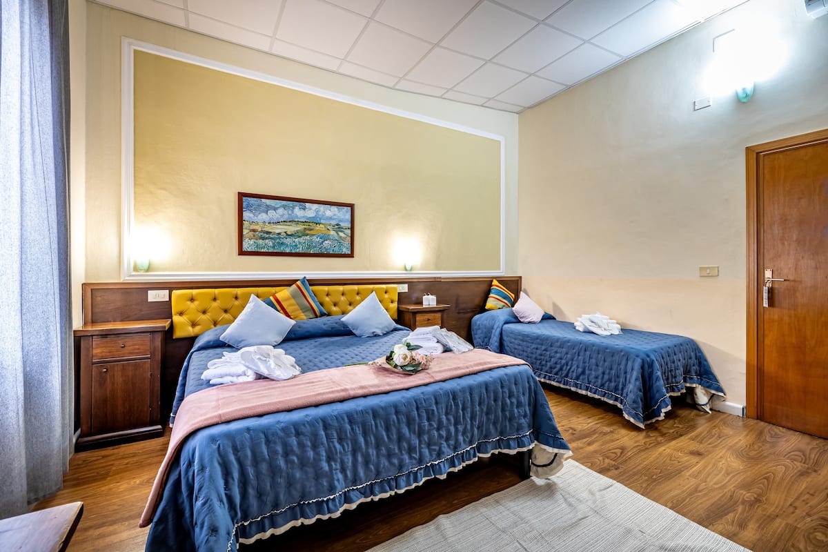 Une chambre d’hôtel avec deux lits, une tête de lit en bois, un tableau au mur et une porte en bois.