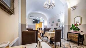 A dining area with tables and chairs, a chandelier, and a television on the wall. - Hotel Minerva (Pisa)