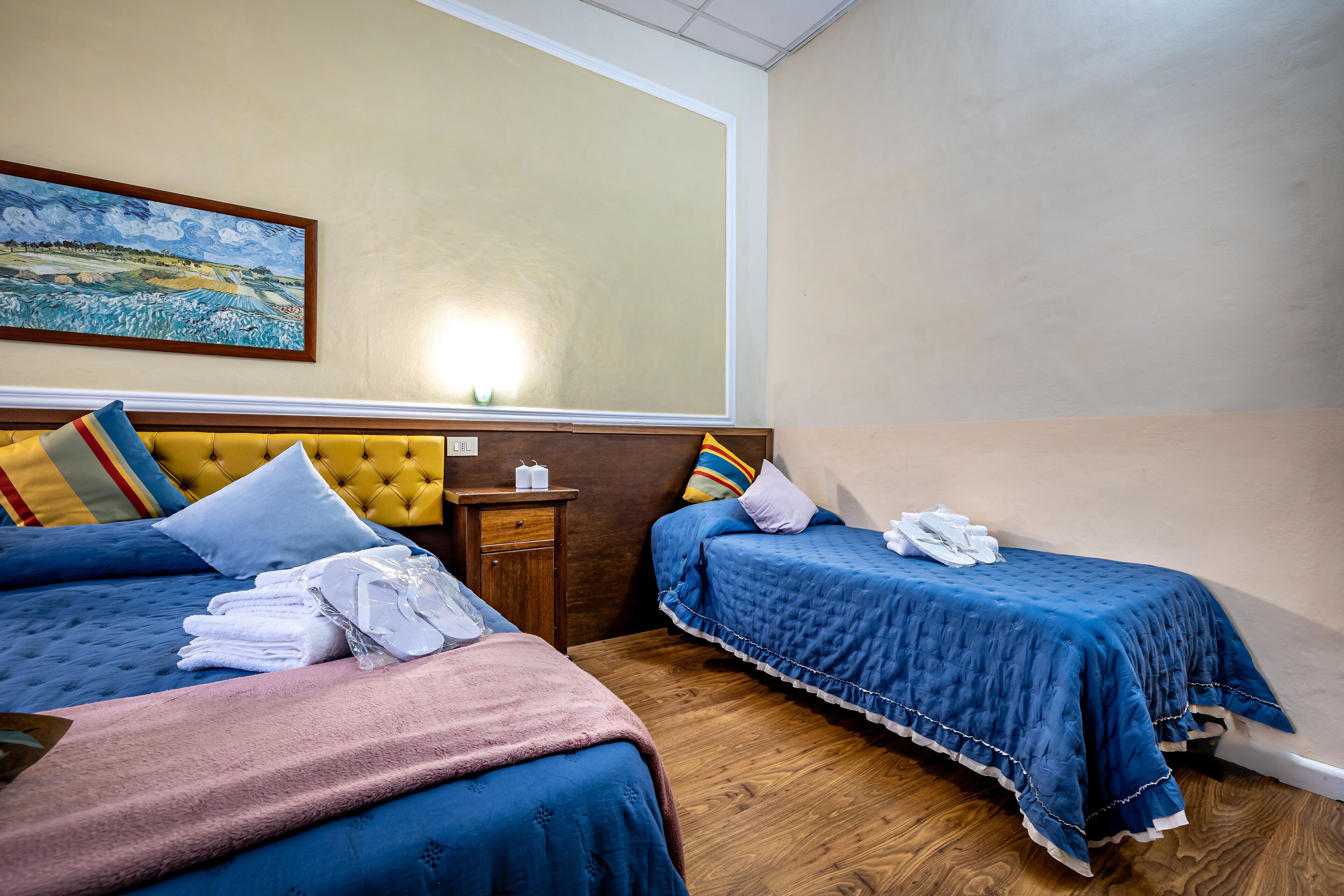 A hotel room with two beds, a wooden headboard, a painting on the wall, and a bedside table with towels.