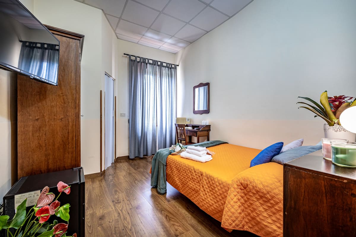 Une chambre d’hôtel avec un lit, un bureau, une chaise, un miroir et une plante.