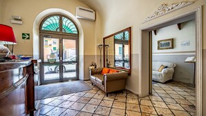 A lobby with a tiled floor, a sofa, a mirror, and a door leading outside. - Hotel Minerva (Pisa)