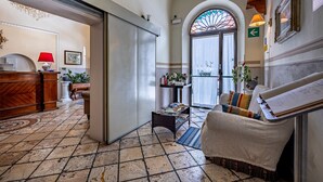 A hotel lobby with a reception desk, a waiting area with a sofa, a staircase, and a large arched window. - Hotel Minerva (Pisa)