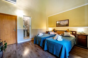 Habitación de hotel con dos camas, suelo de madera, baño visible a través de una puerta abierta y un cuadro enmarcado en la pared.
