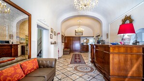 A spacious living area with a leather sofa, a wooden reception desk, and a chandelier. - Hotel Minerva (Pisa)