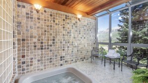 A spa area with a stone mosaic wall, a hot tub, and seating by a large window with a mountain view. - Luxury Lodge with Breathtaking Views (Mountain Village)