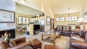 A spacious living room with a fireplace, leather sofas, a coffee table, and a kitchen in the background. - Luxury Lodge with Breathtaking Views (Mountain Village)