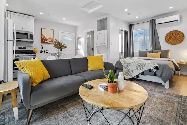 A modern, well-lit living area with a sofa, coffee table, and a bed with a patterned blanket.