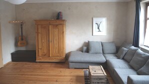 Un salon avec un meuble en bois, un canapé gris, une guitare et un tableau encadré accroché au mur.