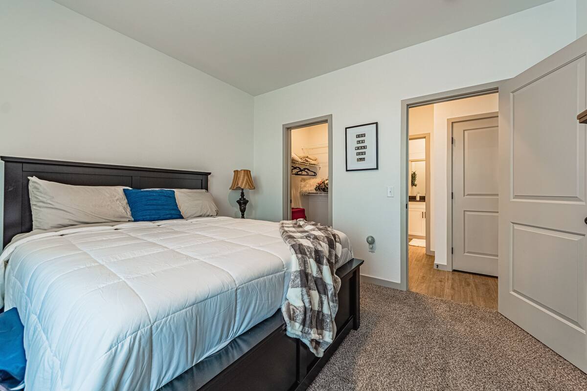 A bedroom with a bed, a bedside lamp, a closet, and a door leading to another room.