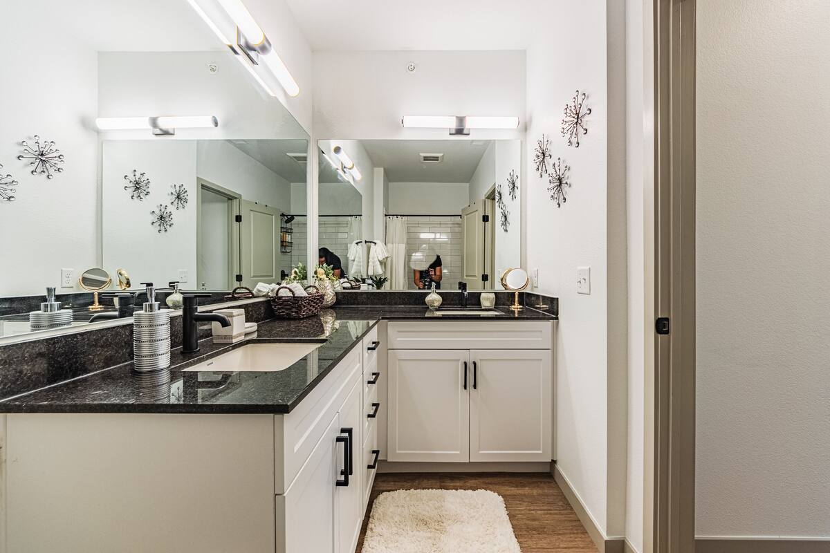 A modern bathroom with a large mirror, white cabinets, and a black countertop.