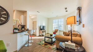 A modern living room with a sofa, coffee table, and a lamp. There is a kitchen area with a refrigerator and a sink. - Beautiful chic modern one bedroom (Colorado Springs)