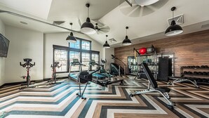 A modern gym with various exercise equipment, large windows, and a chevron-patterned floor. - Beautiful chic modern one bedroom (Colorado Springs)