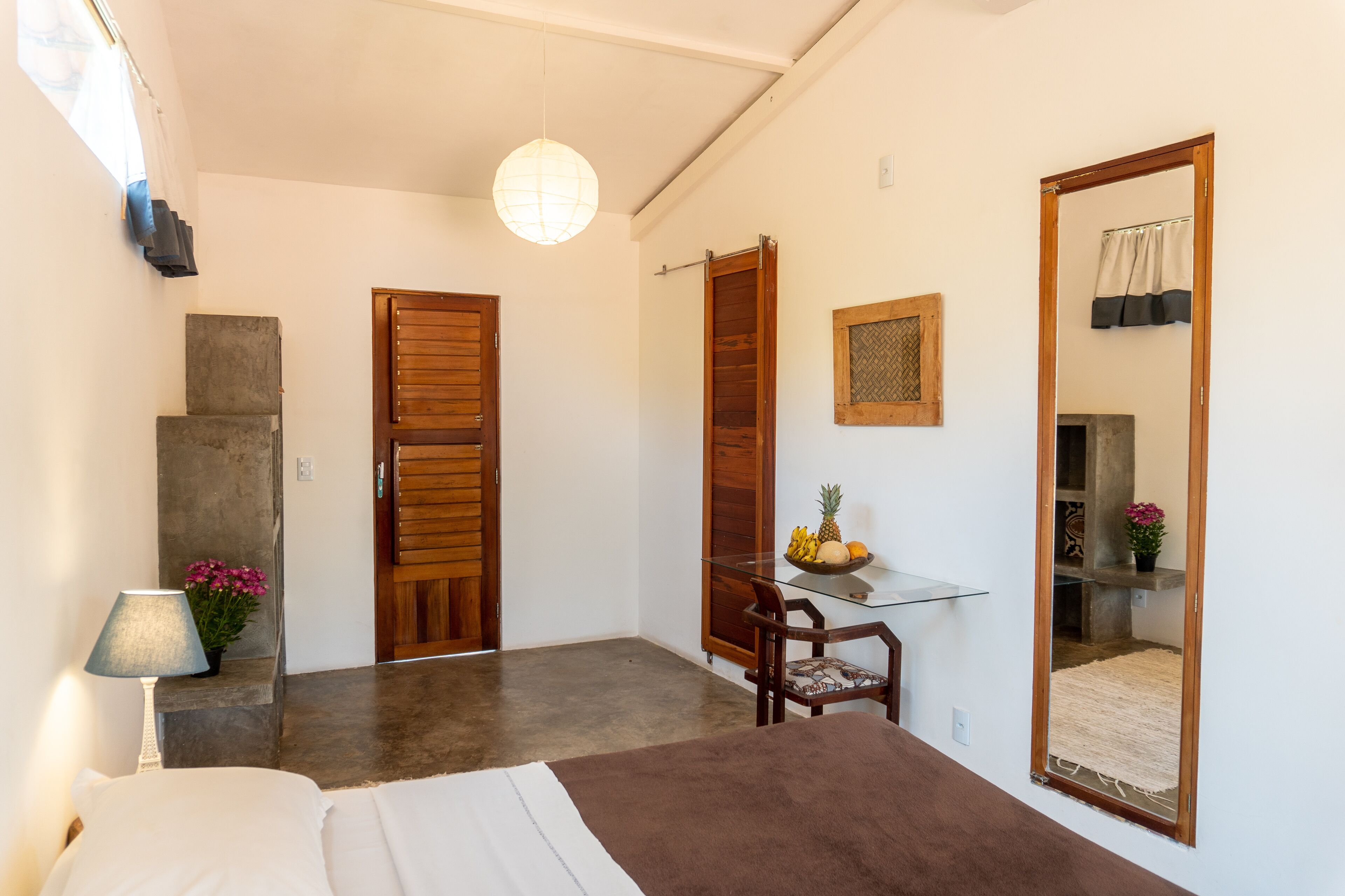 A bedroom with a bed, a glass table with fruit, a chair, and a mirror.