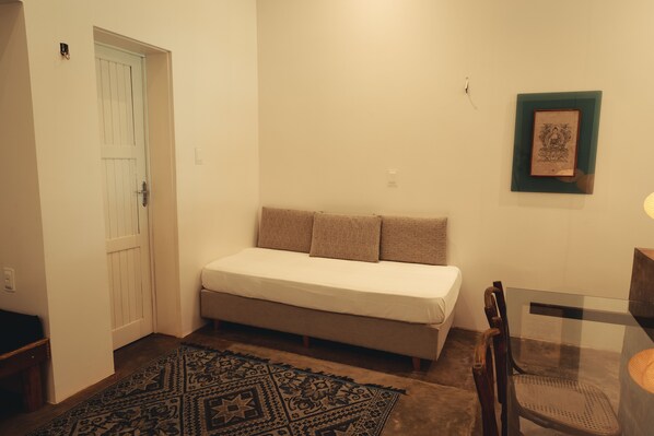 Une pièce comprenant un lit, une table en verre, une chaise, un tapis à motifs et une porte.
