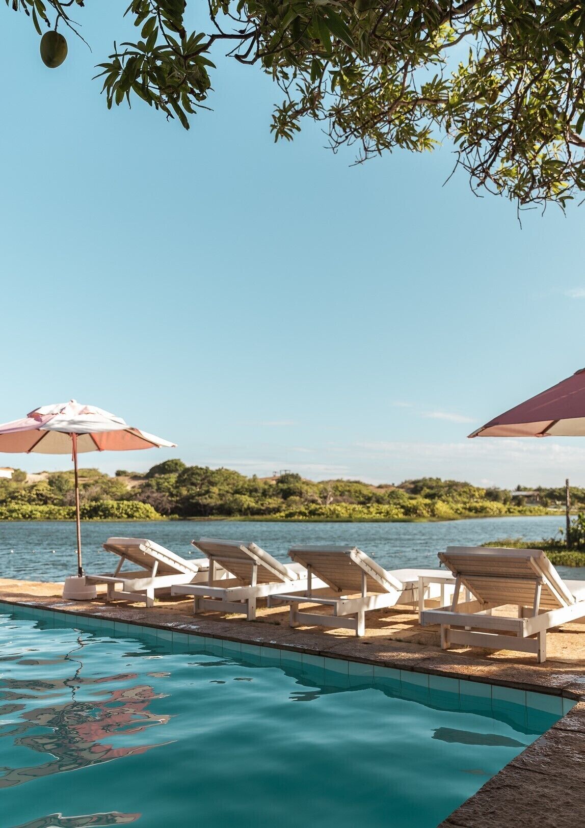 A poolside area with lounge chairs and umbrellas, overlooking a body of water and greenery.