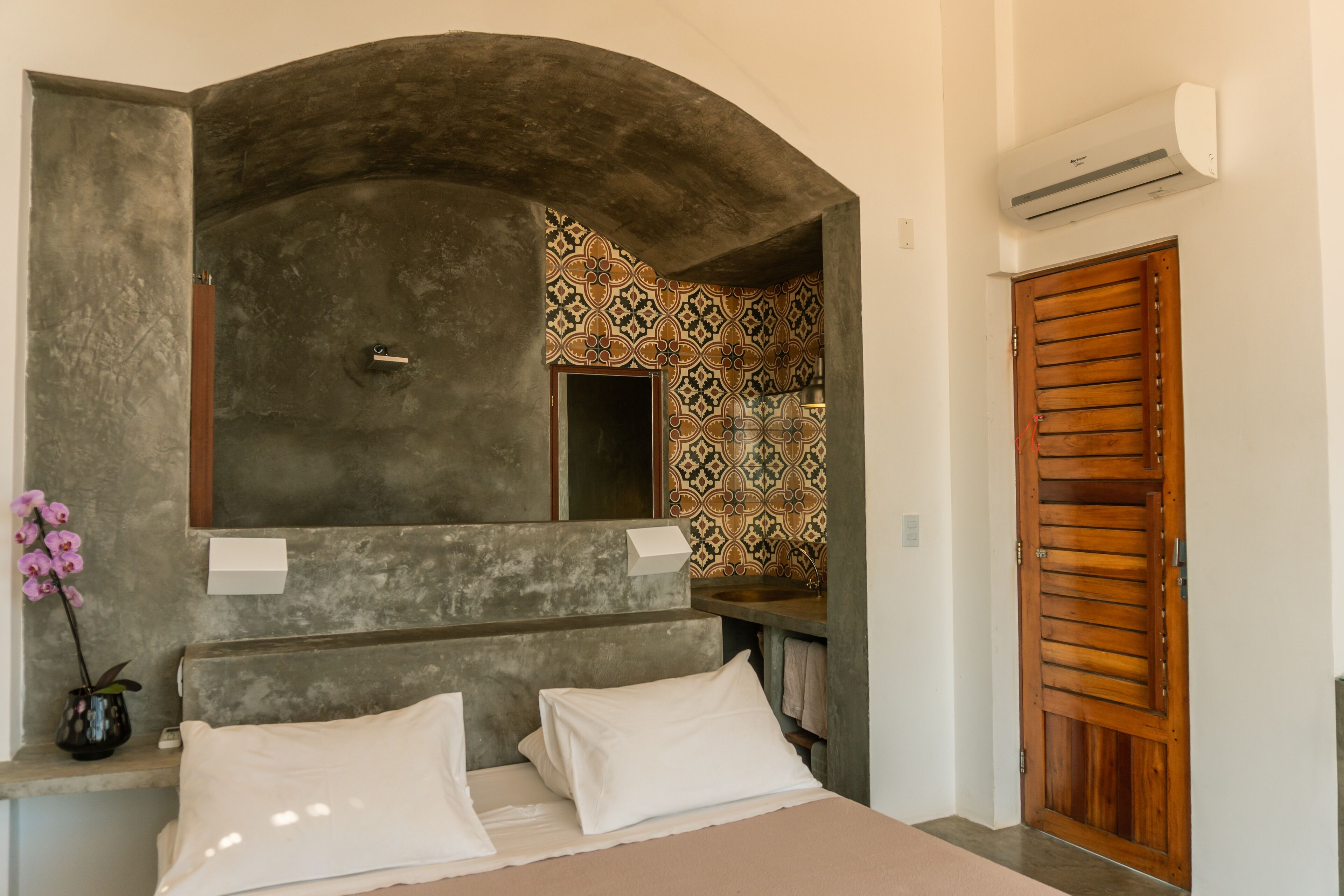 A hotel room with a bed, a mirror, a sink, and a shower area.